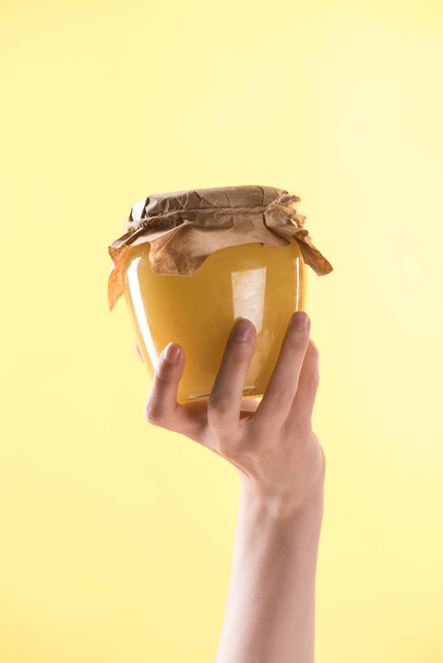 περικομμένη θέα της γυναίκας που κρατά γυάλινο βάζο με νόστιμο μέλι απομονώνεται σε κίτρινο - Φωτογραφία, εικόνα