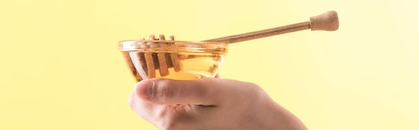 частичный вид женщины, держащей стеклянную чашу с медом и деревянной ковшой, изолированной на желтый, панорамный снимок
 - Фото, изображение