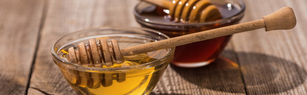 panoramic shot of jars with honey and honey dippers on wooden table in sunlight - Photo, Image