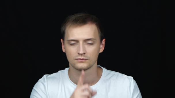 Handsome young caucasian man doing Hush sign with finger on lips, looking at camera. Gesture of Silence on a black background. Quiet sign. Close up portrait. Concept of emotions.  - Footage, Video