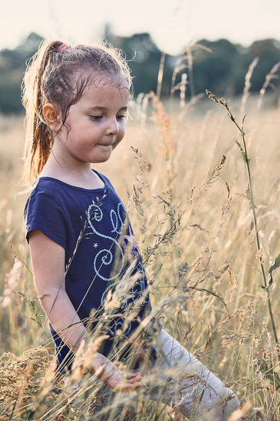 Little happy smiling girl playing in a tall grass - Фото, изображение