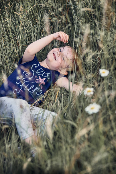 Маленькая счастливая улыбающаяся девочка, играющая на высокой траве
 - Фото, изображение