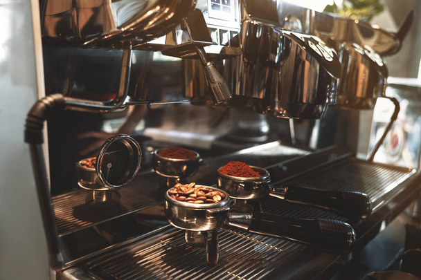 two coffee holders one with fresh ground coffee another with roasted beans standing on professional coffee machine close up - 写真・画像