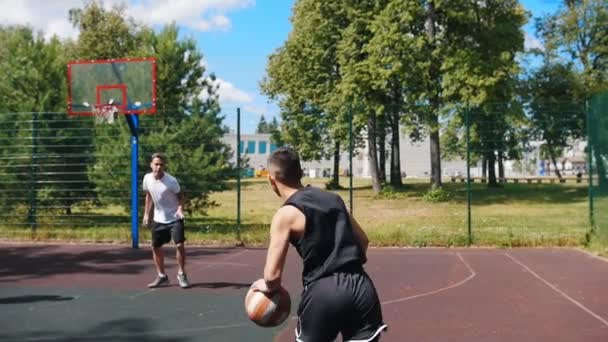 Junger Mann spielt draußen mit Freunden Basketball, dribbelt und verpasst den Korb - Filmmaterial, Video