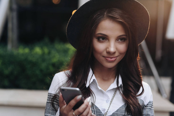 Portrait of good-looking woman with modern black hat look aside using cell phone - Foto, imagen