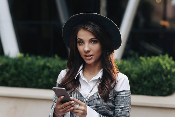 Portrait of stylish woman with modern black hat look aside using cell phone - Φωτογραφία, εικόνα