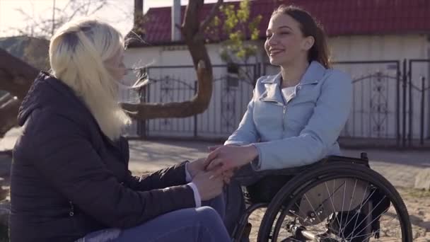 Familienfreizeit. junge behinderte Frau im Rollstuhl spricht mit ihrer Mutter, die am Meer sitzt und sich gegenseitig an den Händen hält - Filmmaterial, Video