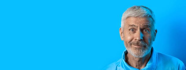 portrait of surprised and curious gray-haired man with a beard on a blue background - Фото, изображение