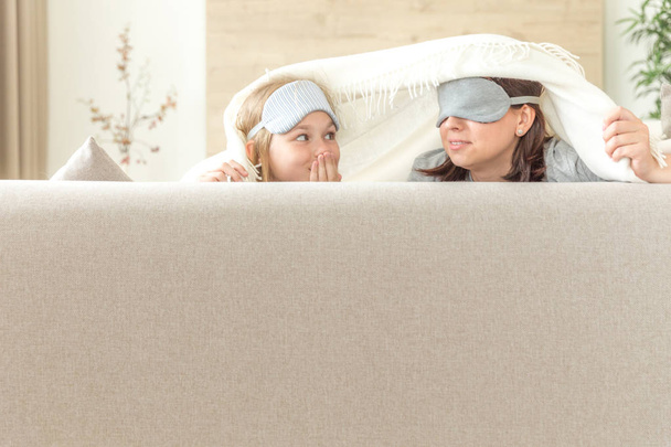 Mother and daughter wearing sleeping mask having fun on couch with copy space - Photo, Image
