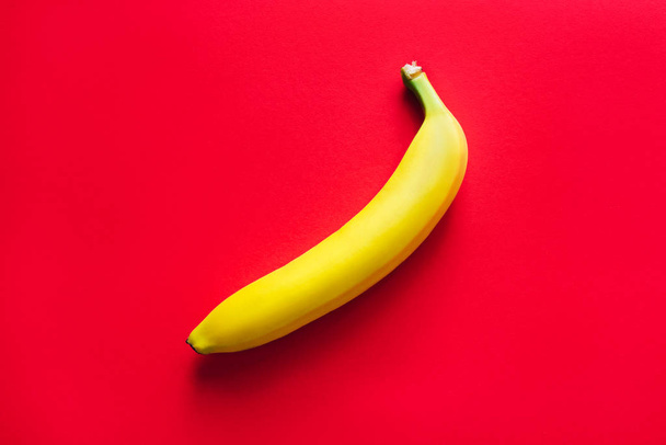 One yellow banana on a red background. - Foto, Imagem