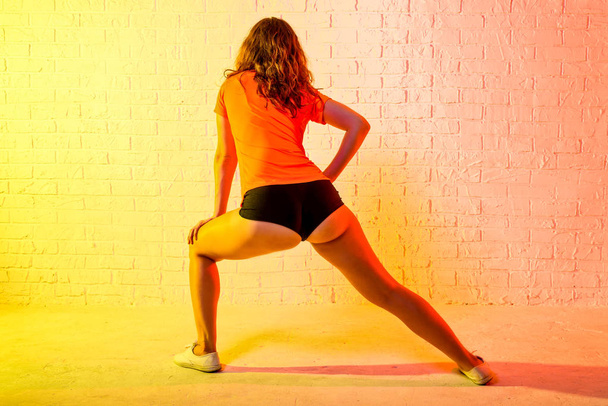 Jonge atletische vrouw doet lunges op een gele achtergrond. - Foto, afbeelding