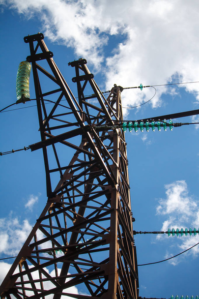 Vue du bas d'un poteau métallique d'une ligne électrique avec une multitude de fils électriques contre un ciel nuageux bleu
 - Photo, image