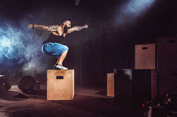 Athlete gave exercise. Jumping on the box. Phase touchdown. Gym shots in the dark tone. Smoke. - Photo, Image