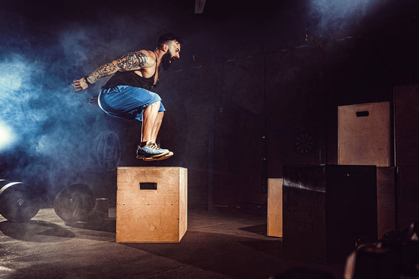 Athlete gave exercise. Jumping on the box. Phase touchdown. Gym shots in the dark tone. Smoke. - Photo, Image