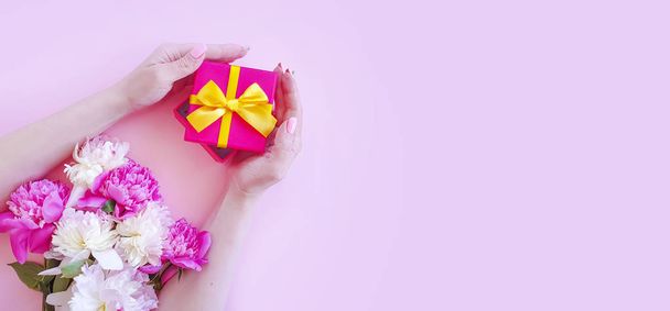 γυναικεία χέρια κρατούν ένα κουτί δώρου, λουλούδι παιωνία σε χρωματιστό φόντο - Φωτογραφία, εικόνα