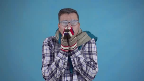 Zamrożony człowiek pokryty mrozem i noszenie rękawiczek i szalik na niebieskim tle - Materiał filmowy, wideo