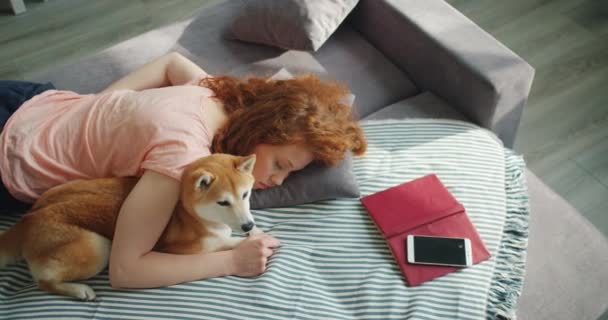 Attractive young woman sleeping at home on sofa hugging cute shiba inu dog - Felvétel, videó