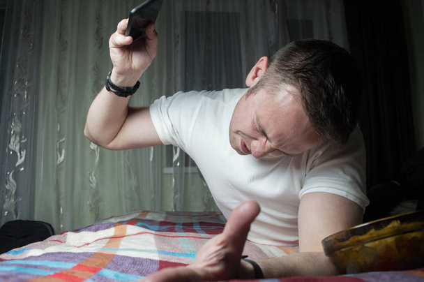 the guy lies at home on the bed and plays a game on the phone - Photo, Image