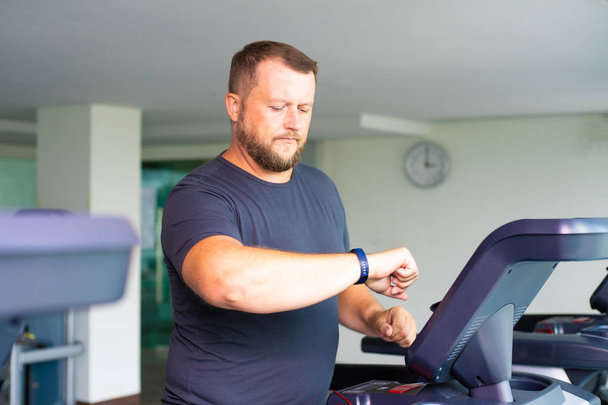 full male runs on a treadmill in the gym and looks at the smart watch. concept of weight loss and sport. side view - Valokuva, kuva