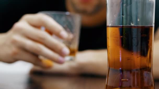 Mladý opilý muž pije whisky ze skleničky a usíná na stole, napůl prázdná láhev whisky v popředí zaostření - Záběry, video
