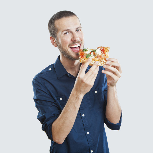 Portrait of a young beautiful man eating a slice of pizza margherita - Photo, Image