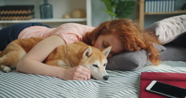 Attractive young woman and cute dog sleeping together at home on bed hugging - Video