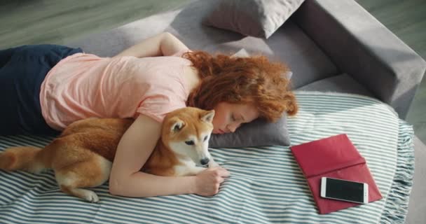 Pretty girl and loyal dog sleeping together on sofa at home relaxing during day - Filmagem, Vídeo