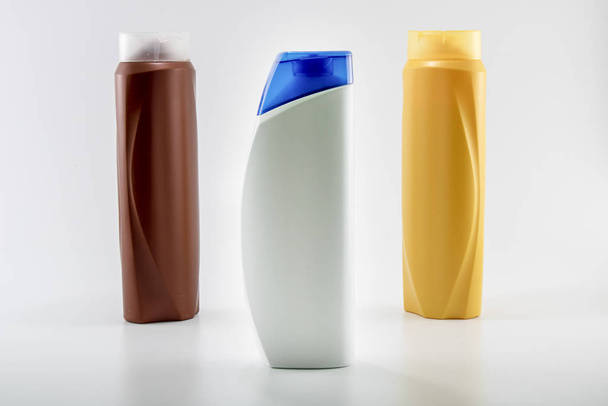 Shampoo, hydraterende flessen in bruine, witte, gele kleuren. Fotograferen in witte achtergrond. Met blauwe dop in het midden - Foto, afbeelding