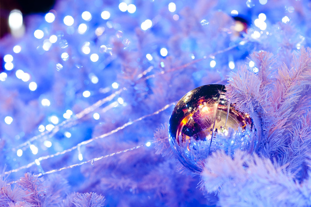 A close up image of a white decorative Christmas ornamental orb on a white fir tree branch with the blue lighting. - Фото, изображение
