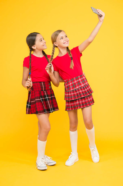family bonding. sisterhood and friendship. happy knowledge day. childhood happiness. education concept. back to school. social network. girls in uniform. small girls make selfie on phone. having fun - Foto, imagen