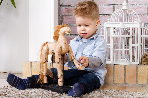 Little boy sits on a floor with toy horse - Foto, afbeelding
