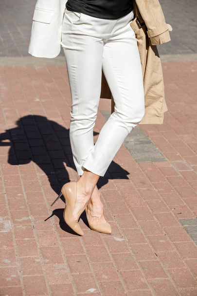 Beauty woman standing outdoors at daytime. Cropped shot of stylish model wearing white pants and heels  - Photo, image