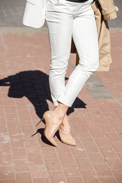 Beauty woman standing outdoors at daytime. Cropped shot of stylish model wearing white pants and heels  - Φωτογραφία, εικόνα