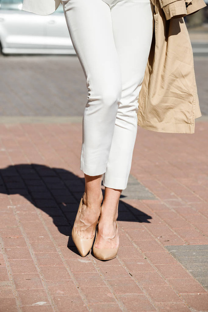 Mujer de belleza de pie al aire libre durante el día. Recortado tiro de modelo elegante con pantalones blancos y tacones
  - Foto, imagen