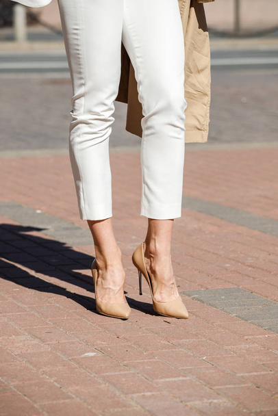 Beauty woman standing outdoors at daytime. Cropped shot of stylish model wearing white pants and heels  - Foto, imagen