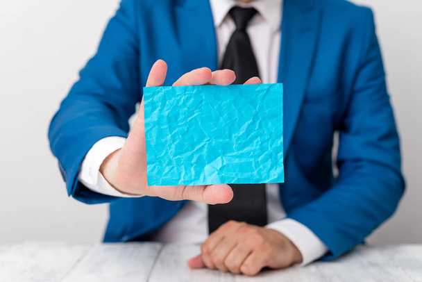 Man holds empty blue paper with copy space in front of him. Business concept with man in a suite and a tie. Blue space for advertising message. - Φωτογραφία, εικόνα
