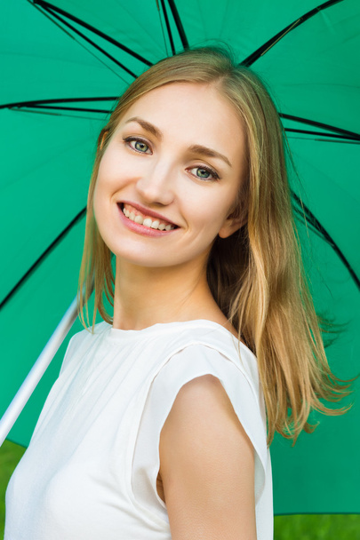 Young smiling girl holding a green umbrella - Foto, afbeelding