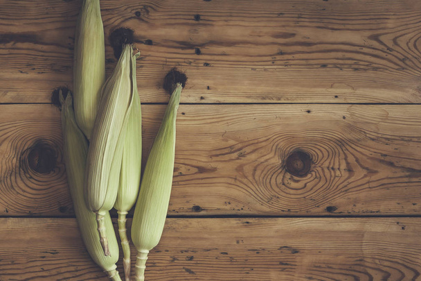 Świeże kolby surowe kukurydzy na drewnianym tle. Kukurydza surowa ze skórą - Zdjęcie, obraz