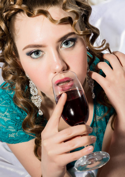 beautyful young curly woman resting on the bed in a hotel room and enjoying red wine - Fotografie, Obrázek