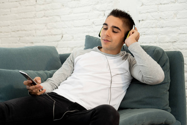 Portrait of young happy teenager male listening to music in headphones singing and dancing on sofa at home. In positive emotions, youth and happiness,Leisure Music and technology concept. - Foto, Imagen