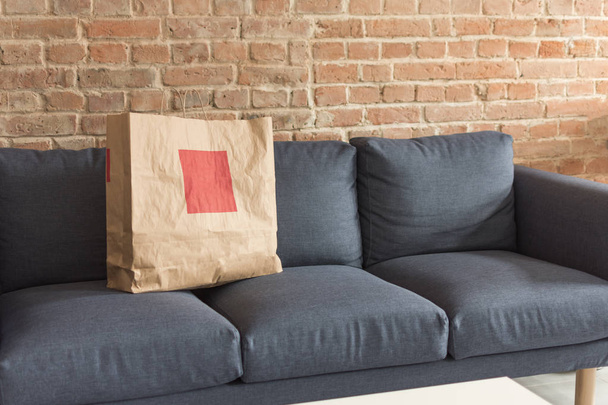 Blank paper gift or shopping bag standing on blue modern sofa. - Zdjęcie, obraz