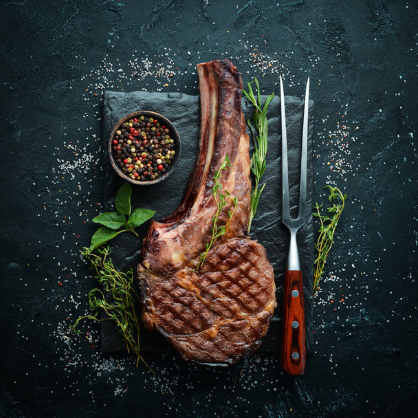 Grilled cowboy beef steak, herbs and spices on a black stone background. Barbecue. Top view. Free space for text. - Fotó, kép