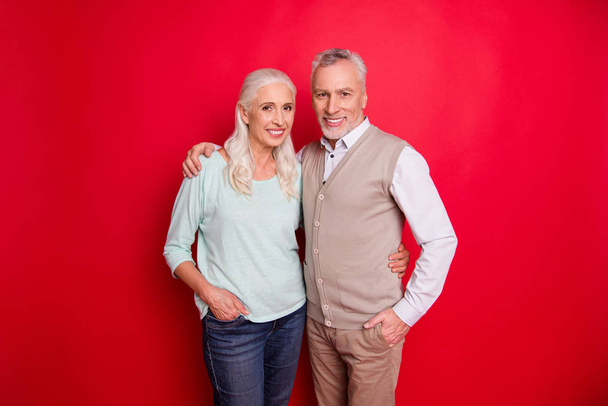 Close up photo funny amazing beautiful she her he him his old guy lady standing hugging sincere beaming smile easy-going best partners wear sweater pullover shirt waistcoat isolated red background - Valokuva, kuva