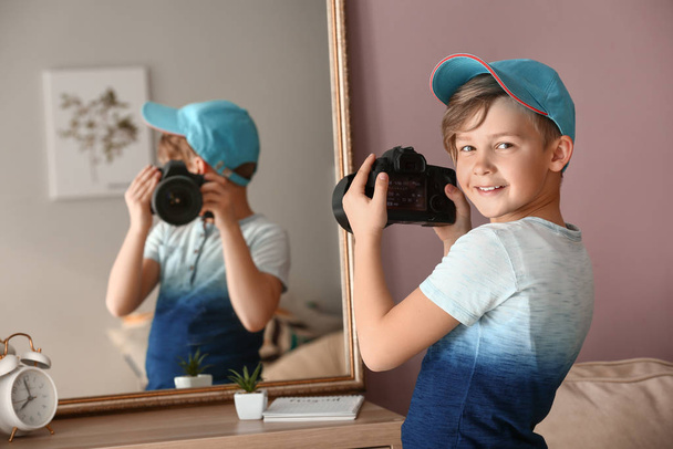 Schattige kleine fotograaf met professionele camera in de buurt van spiegel thuis - Foto, afbeelding