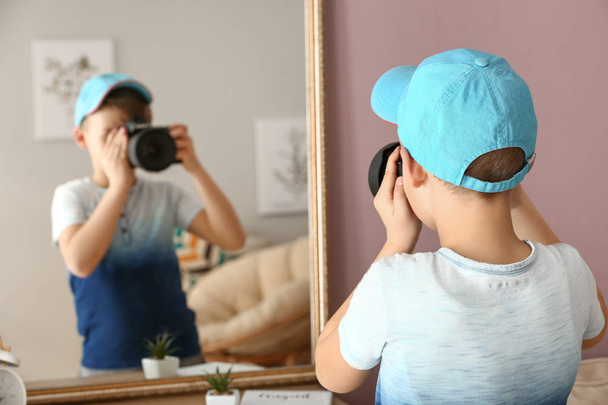 自宅で鏡の近くにプロのカメラを持つかわいい小さな写真家 - 写真・画像