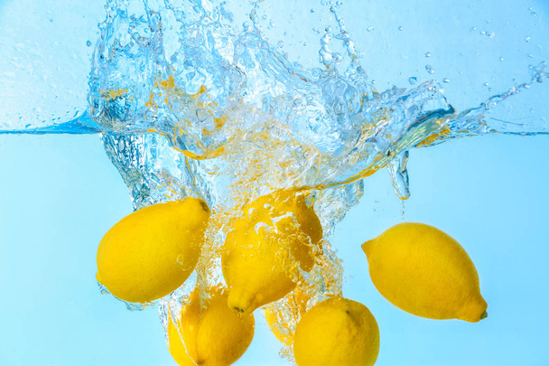 Vallen van citroenen in water op lichte achtergrond - Foto, afbeelding
