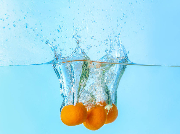 Falling of tangerines into water on light background - Photo, Image