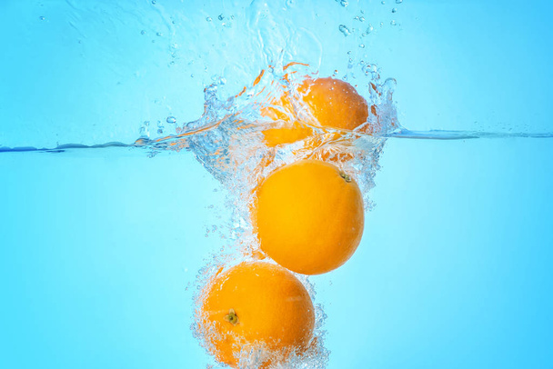 Falling of oranges into water on light background - Photo, Image