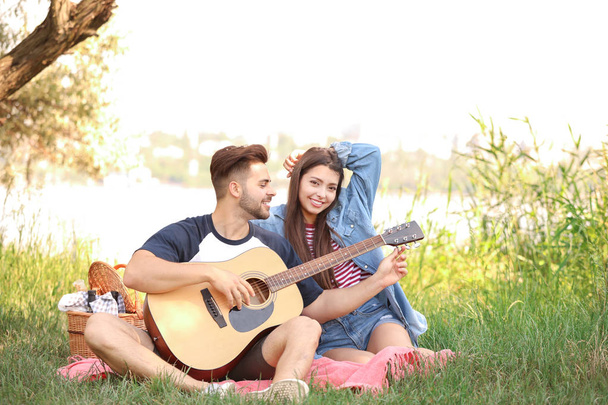 Jovem casal com guitarra em piquenique no parque
 - Foto, Imagem