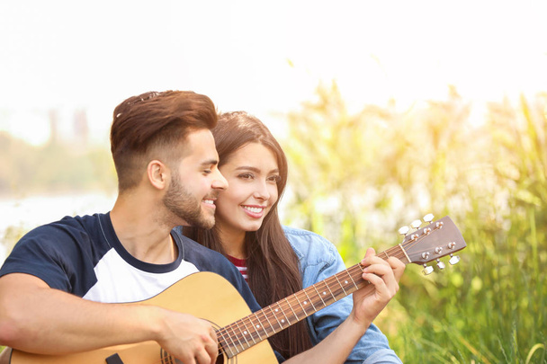 Young couple with guitar on picnic in park - Foto, afbeelding